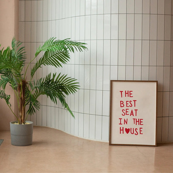 Plakat med rød tekst “The Best Seat in the House” og hjerte – humoristisk vægkunst til badeværelse eller gæstetoilet, indrammet og opstillet i moderne interiør.
