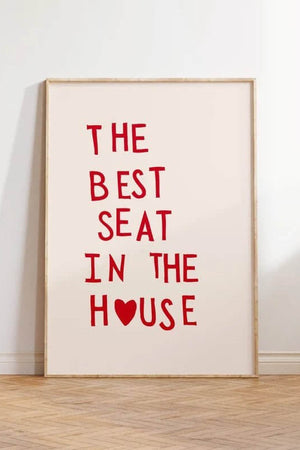 Plakat med rød tekst “The Best Seat in the House” og hjerte – humoristisk vægkunst til badeværelse eller gæstetoilet, indrammet og opstillet i moderne interiør.