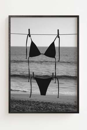 Sort-hvid strandplakat med sort bikini hængende foran havet.