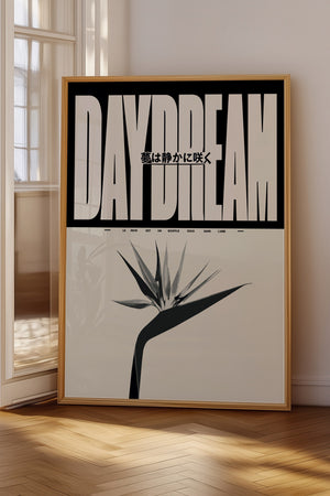 Daydream plakat med stor beige typografi, japansk tekst og stiliseret blomst i egetræsramme på gulv ved vindue