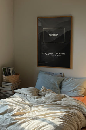 Grind plakat med bjerglandskab i gråsorte nuancer og hvid typografi i egetræsramme over seng