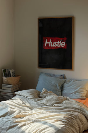 Hustle plakat med hvid slidt typografi på mørkerød tekstureret baggrund i egetræsramme over seng