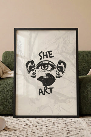 She Art plakat med grafiske ansigtsdetaljer og tekst i sort hvid i egetræsramme ved sofa